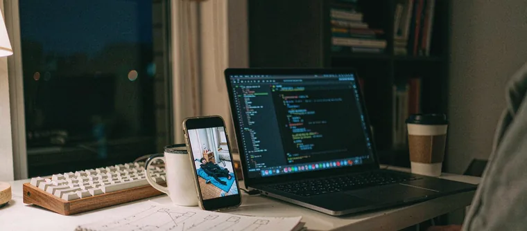 A developer desk at night with a phone playing a vertical video beside a laptop